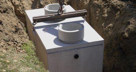 Concrete utility box in a rocky trench with a round vent on top.