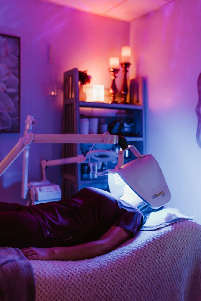 A woman is laying on a bed with a lamp on her face.