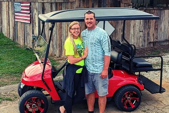 A man and a woman are standing next to a red golf cart.