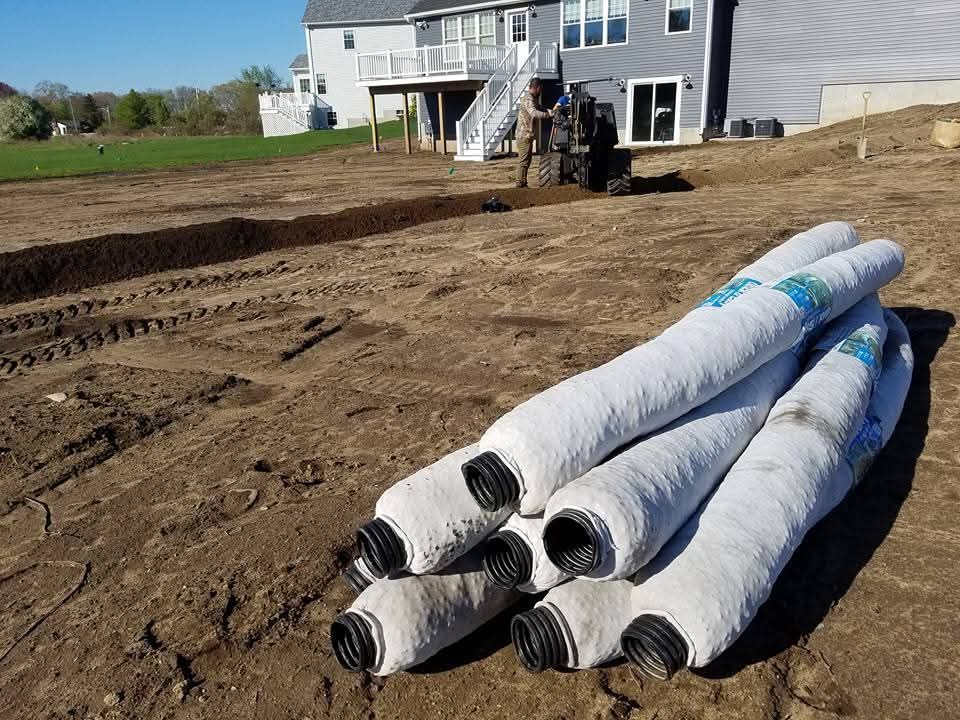 A pile of drain pipes sitting on top of a dirt field in front of a house.