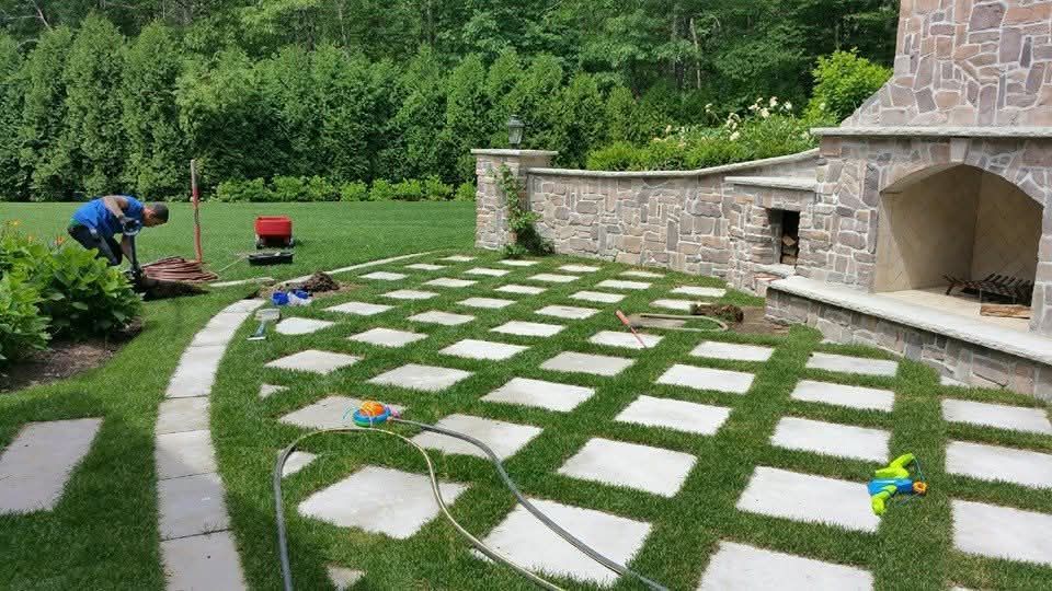 A man is planting a tree in a backyard next to a stone fireplace.