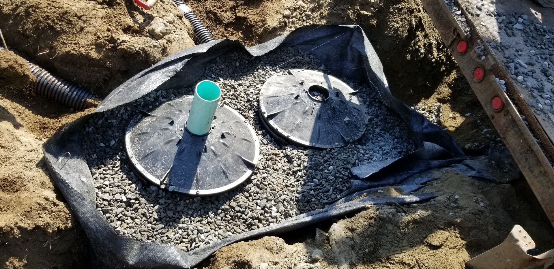 A green pipe is sitting on top of a black tarp in the dirt.