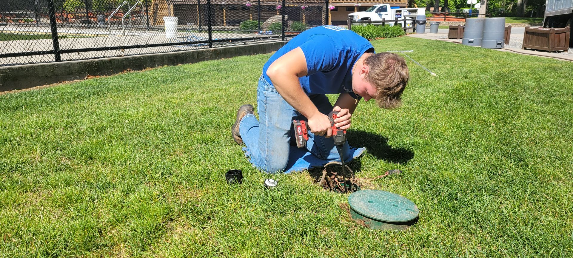 A man is kneeling down in the grass using a drill.