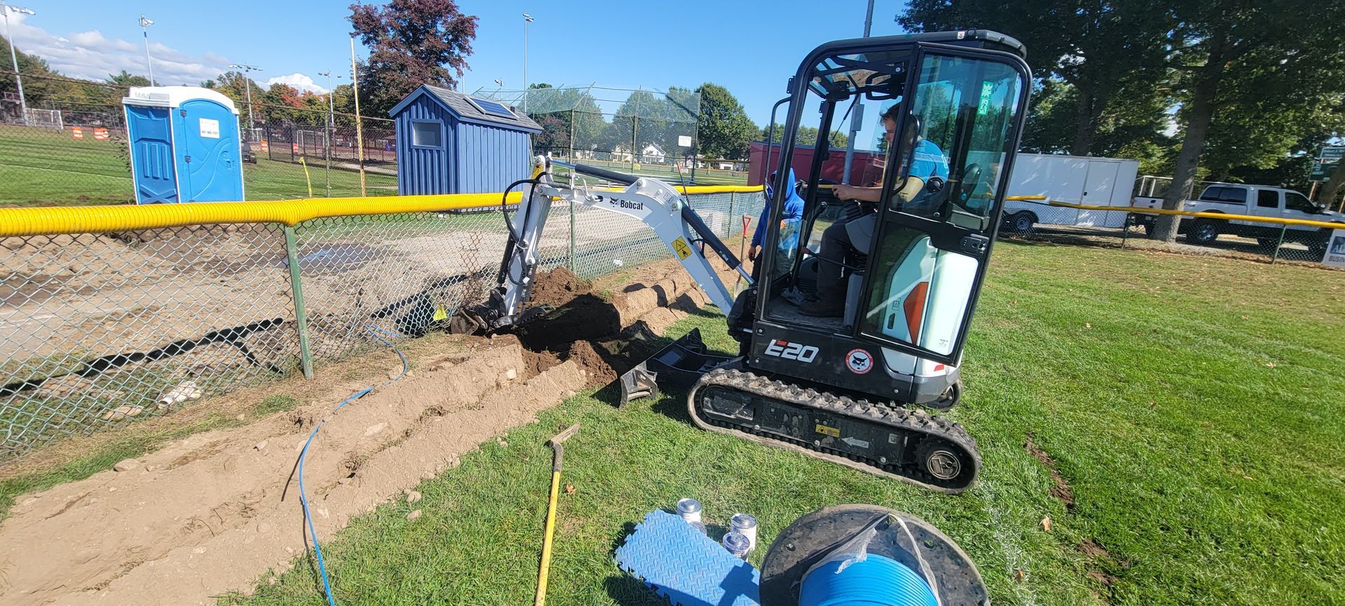 A small excavator is digging a hole in the grass in a park.