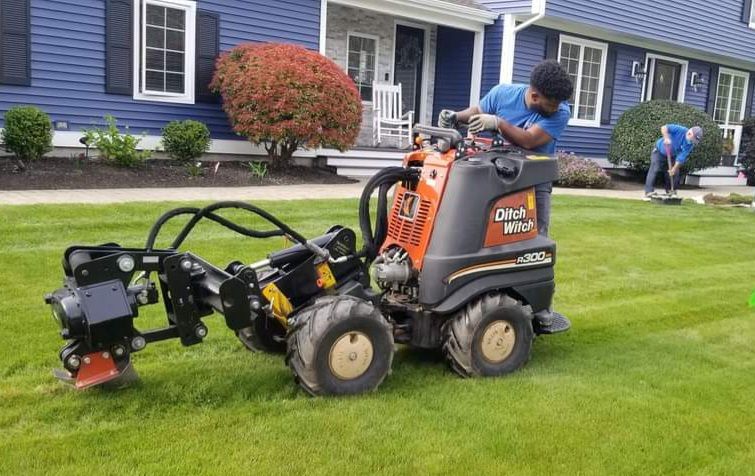 A man is driving a tractor on a lush green lawn in front of a house.