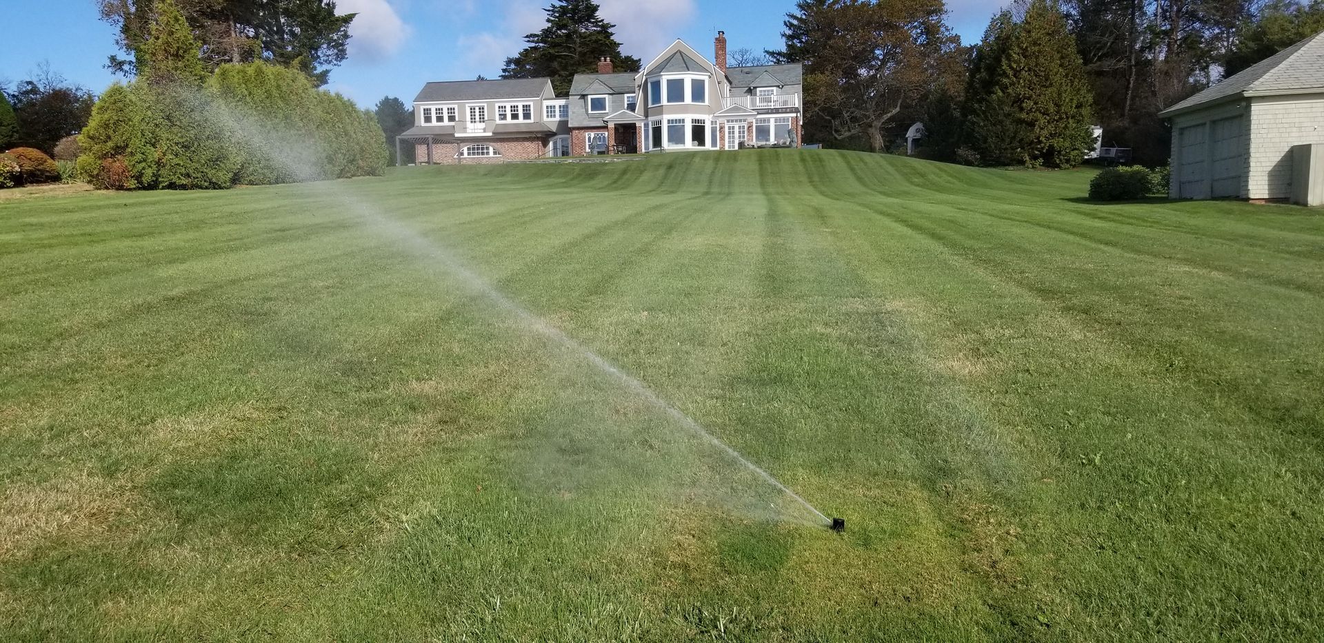 A lawn sprinkler is spraying water on a lush green lawn in front of a house.