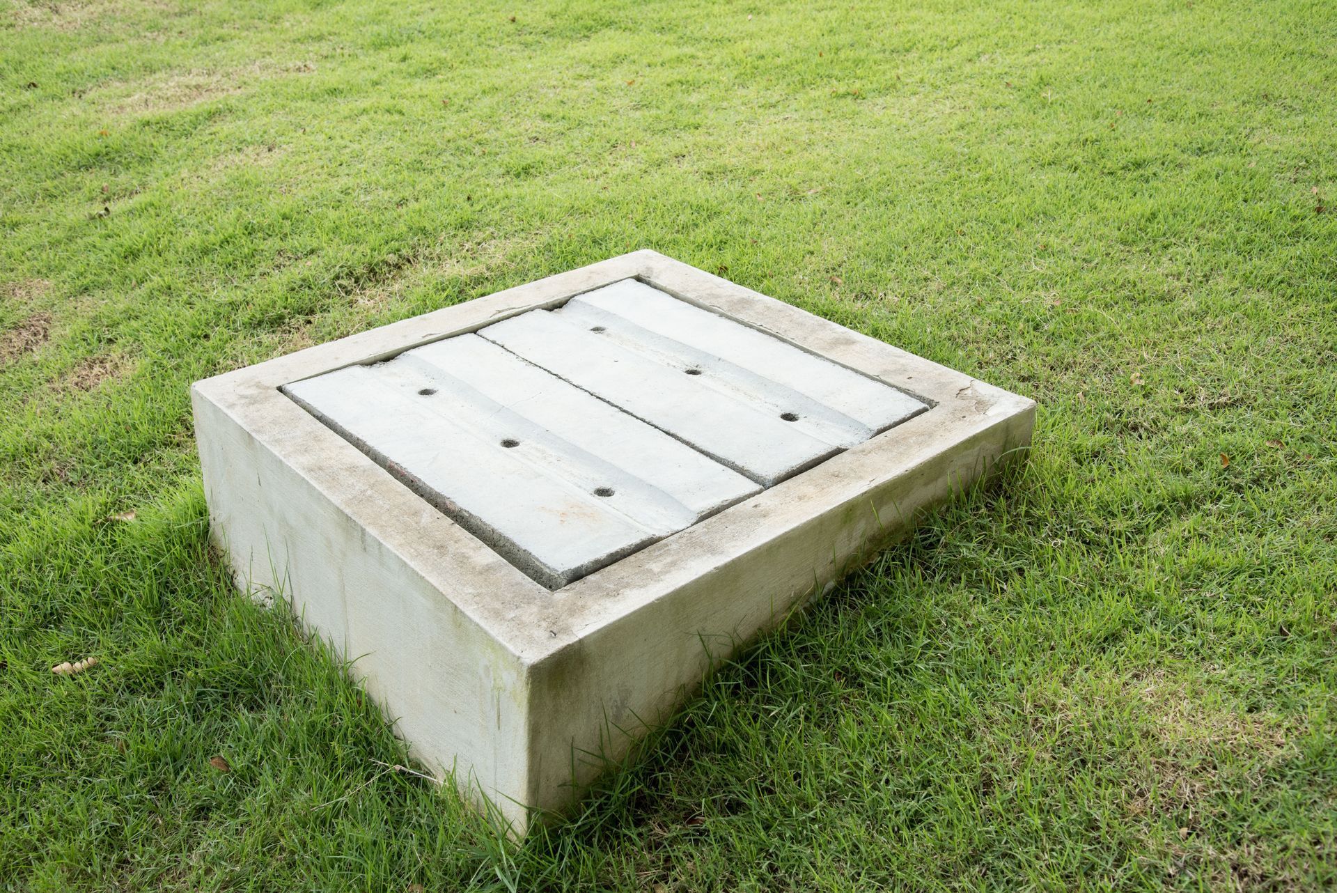 Concrete rectangular utility access box with a lid, set in grass.