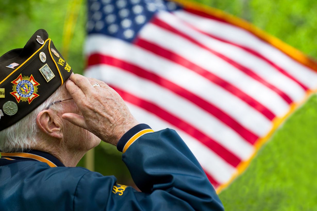 Veteran salutes the American flag, outdoors on a sunny day.