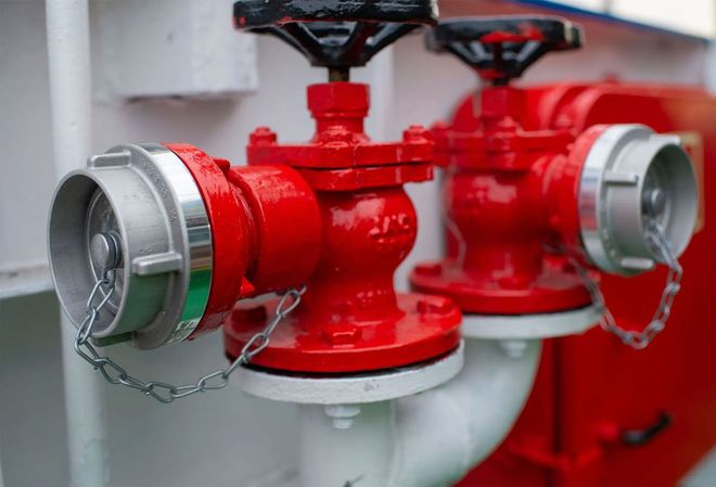 Red fire hydrant valves with silver caps and chains in a utility room