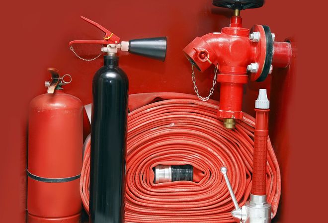 Red and black fire extinguishers and a coiled red hose against a red wall