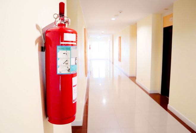 Red fire extinguisher mounted on a wall in a bright hallway.