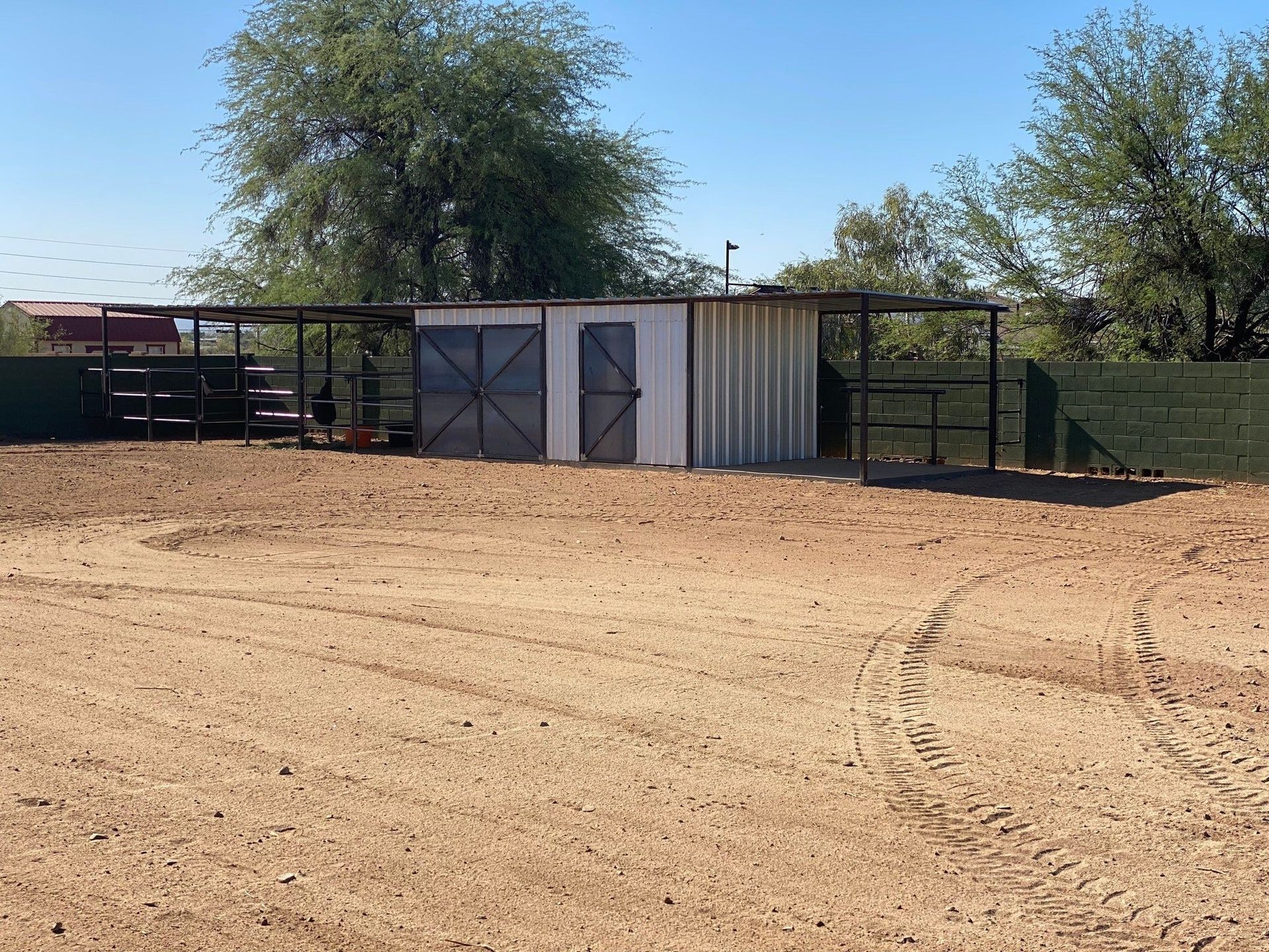 A dirt lot with a metal shelter. Two doors are centered, with fenced areas on either side.
