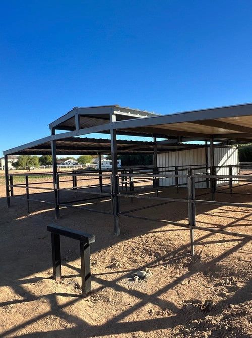Metal horse stalls and covered shelter under a clear blue sky.