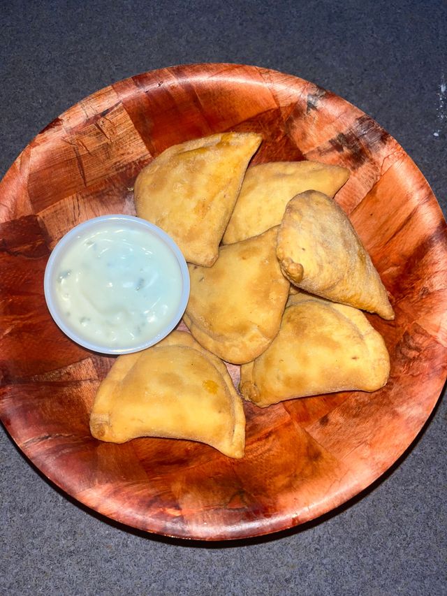 Plate of golden fried pastries with a small cup of white dipping sauce