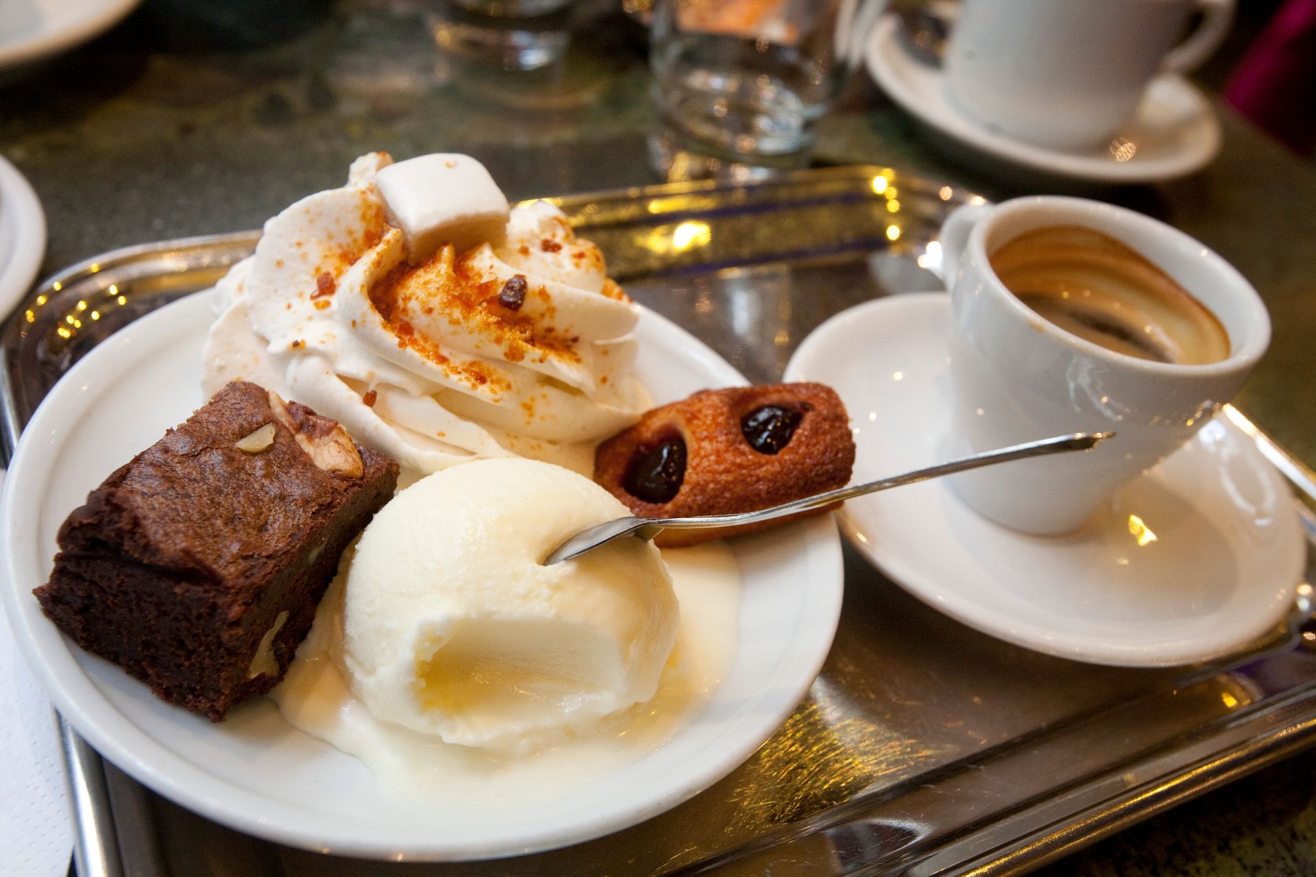 Assorted desserts on a white plate with coffee on a tray, including cake, ice cream, and a spoon.