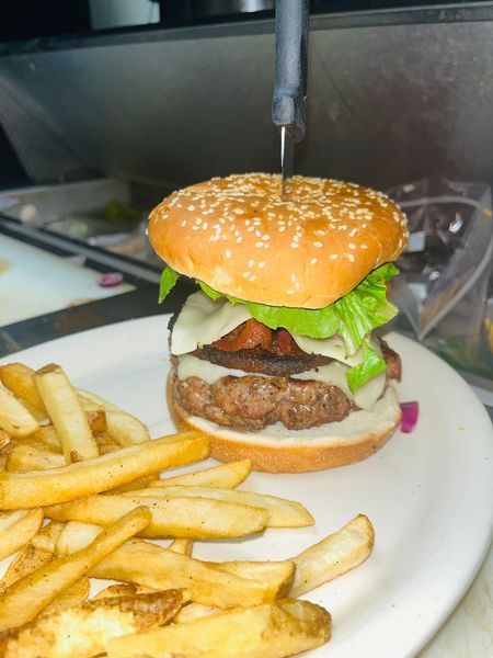 Burger with sesame bun and fries on a white plate, with a fork or skewer above it
