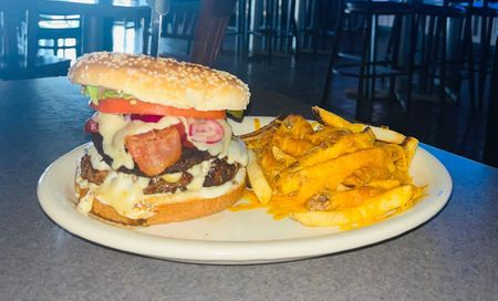 Burger and seasoned fries on a white plate in a dimly lit restaurant.
