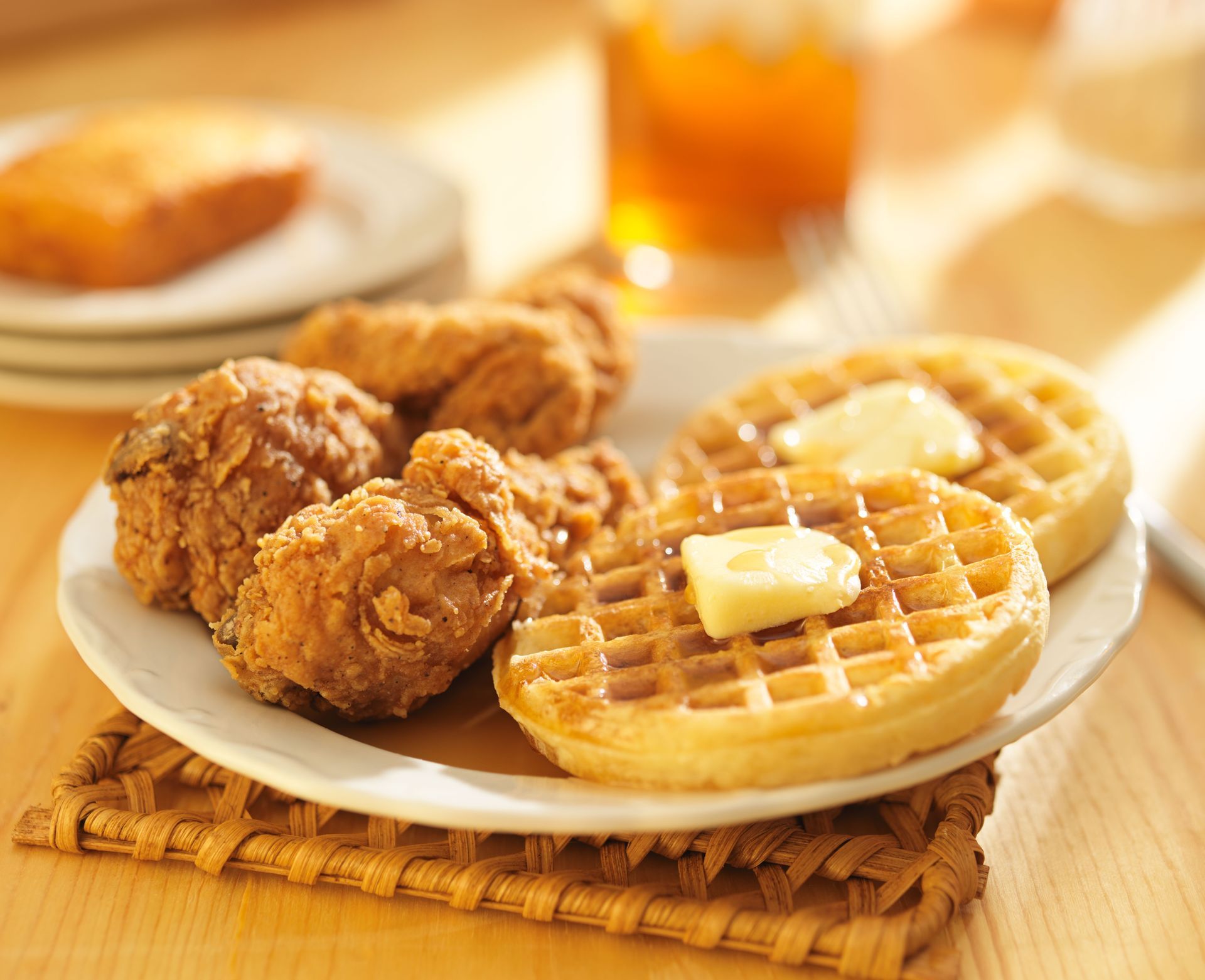 Fried chicken and waffles on a white plate with syrup and butter on a woven placemat.
