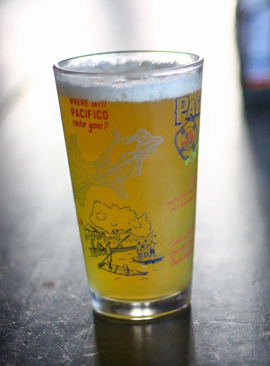 Yellow drink in a clear glass on a dark table, with red text and a small cartoon graphic.