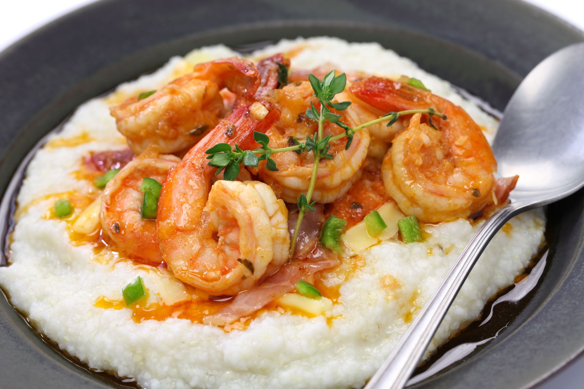 Shrimp and tomato sauce over creamy grits in a dark bowl, garnished with herbs and a spoon nearby