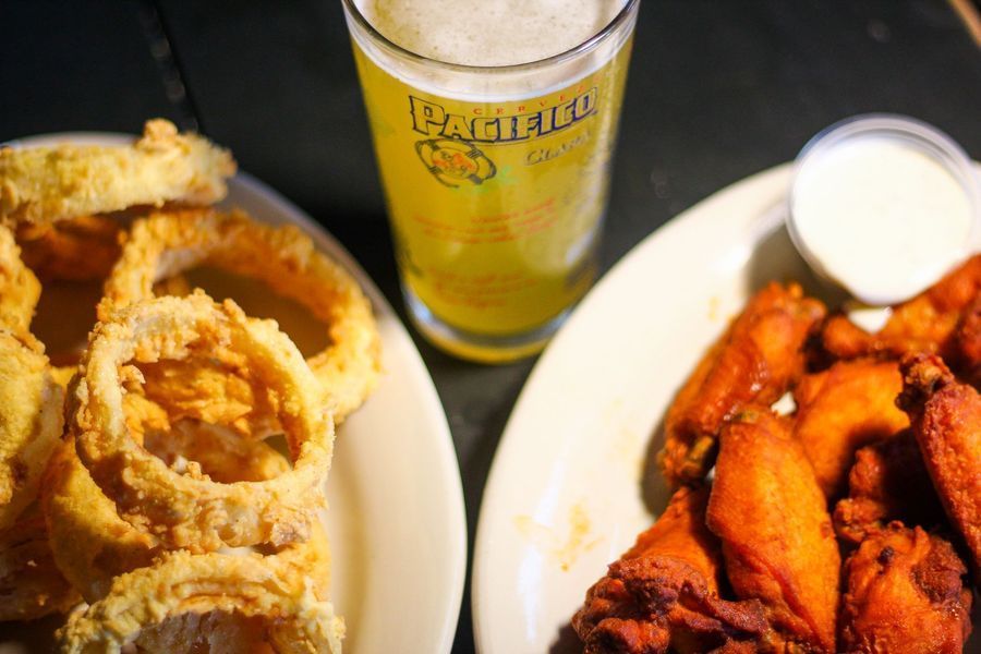 Plate of onion rings and fried wings with a beer on a table