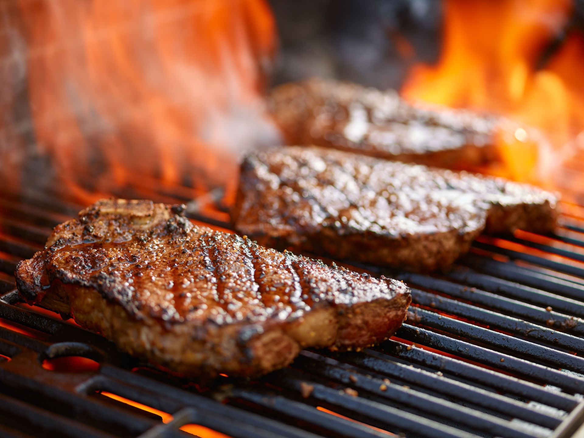 Steaks grilling on a barbecue with flames and glowing coals