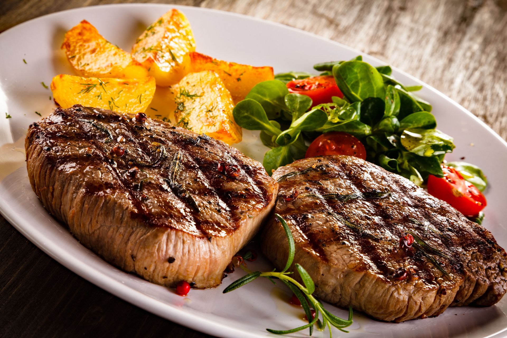 Grilled steaks with roasted potatoes and a green salad on a white plate