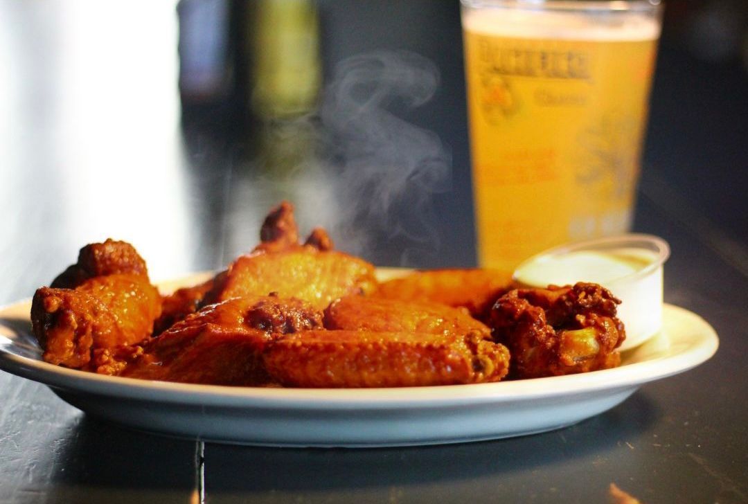 Plate of fried chicken wings with dipping sauce and a drink in the background on a table