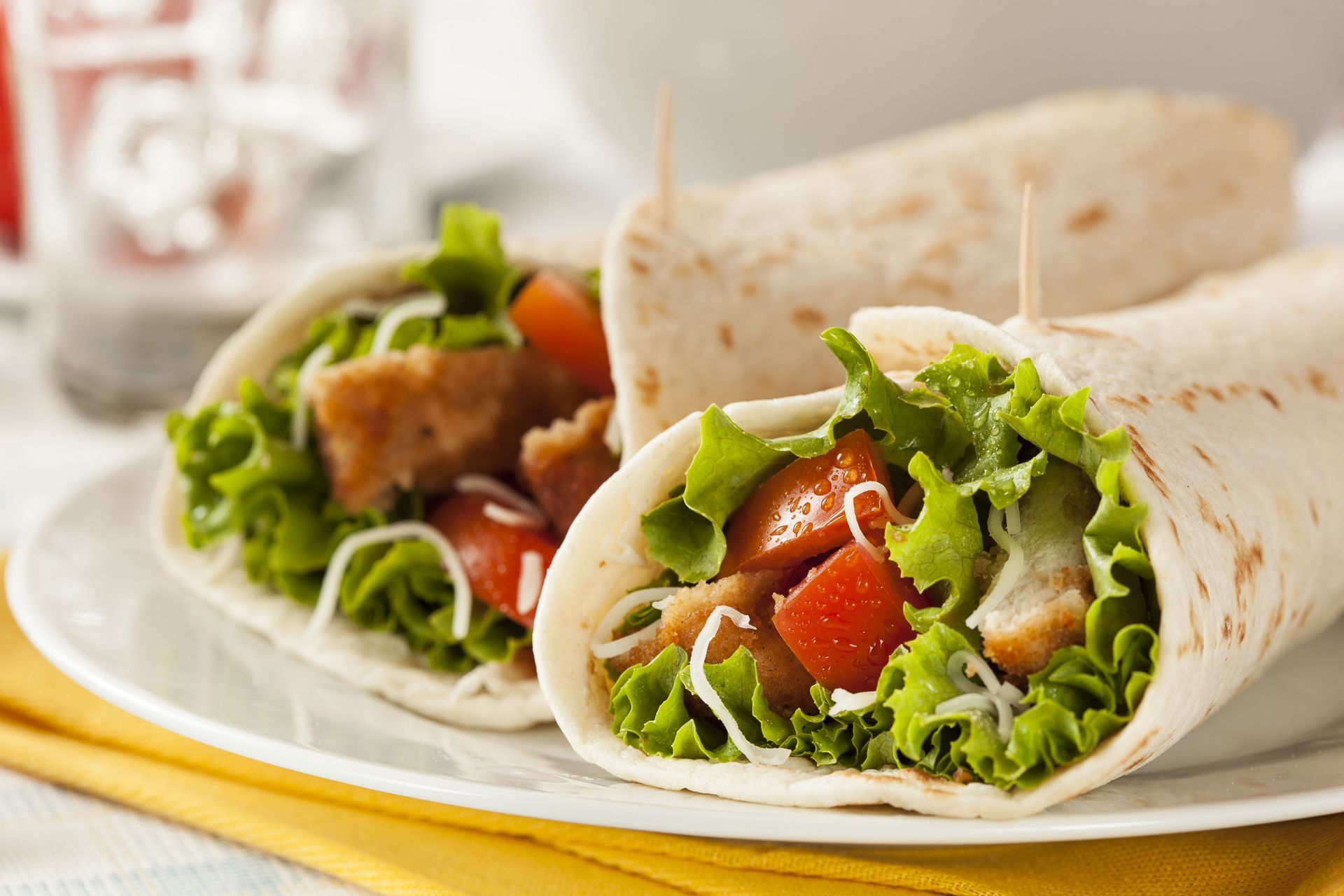 Chicken wraps with lettuce and tomatoes on a white plate, served on a yellow napkin