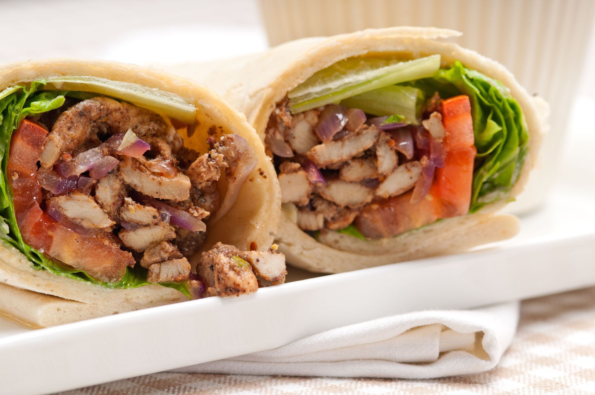 Close-up of two grilled chicken wraps with lettuce and tomatoes on a white plate