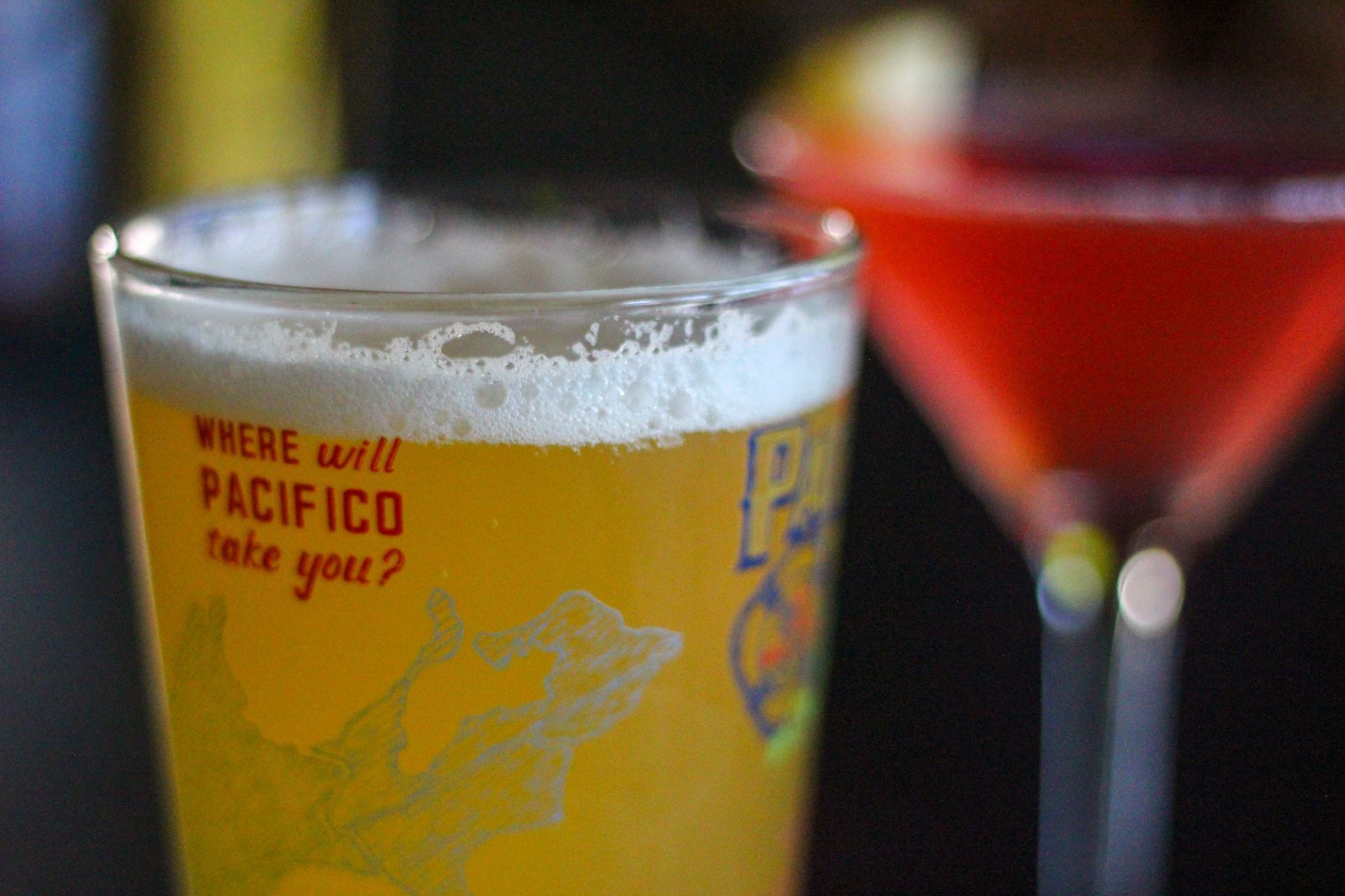 Two cocktail glasses: a frothy yellow drink in front and a red martini behind.