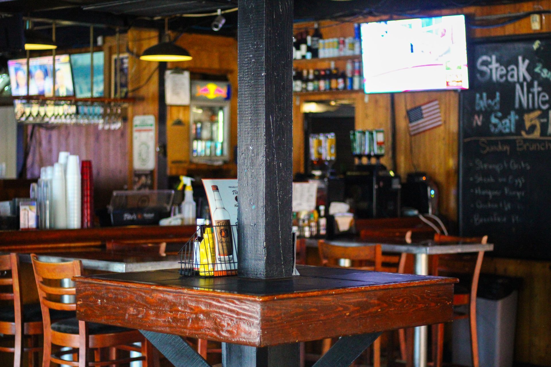 Empty bar interior with wooden tables, stools, TVs, and a chalkboard menu