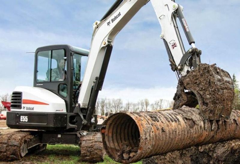 A bobcat excavator is digging a hole for a pipe