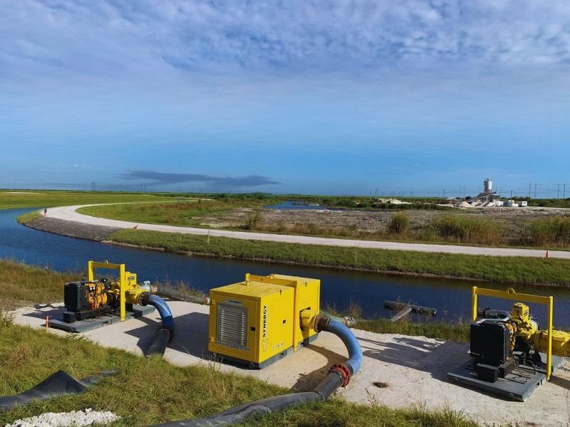 A row of yellow pumps are sitting next to a river.