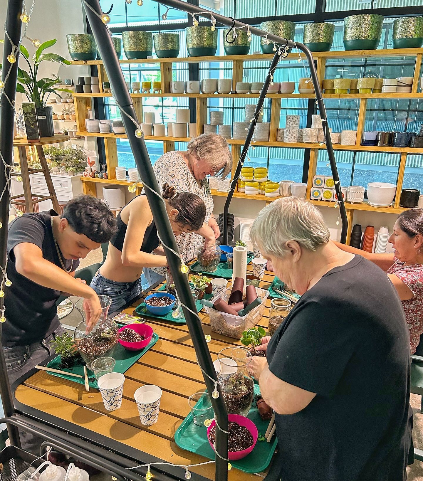 A group of people are sitting around a table working on potted plants.