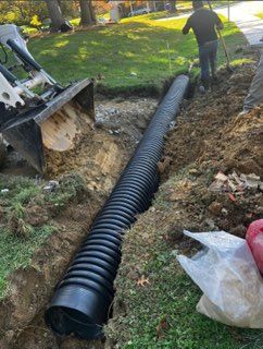 A man is standing next to a large black pipe in the dirt.