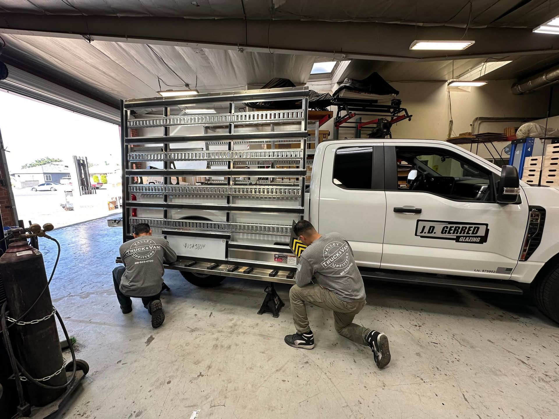 Two people working on a white truck with a custom storage unit in a garage.