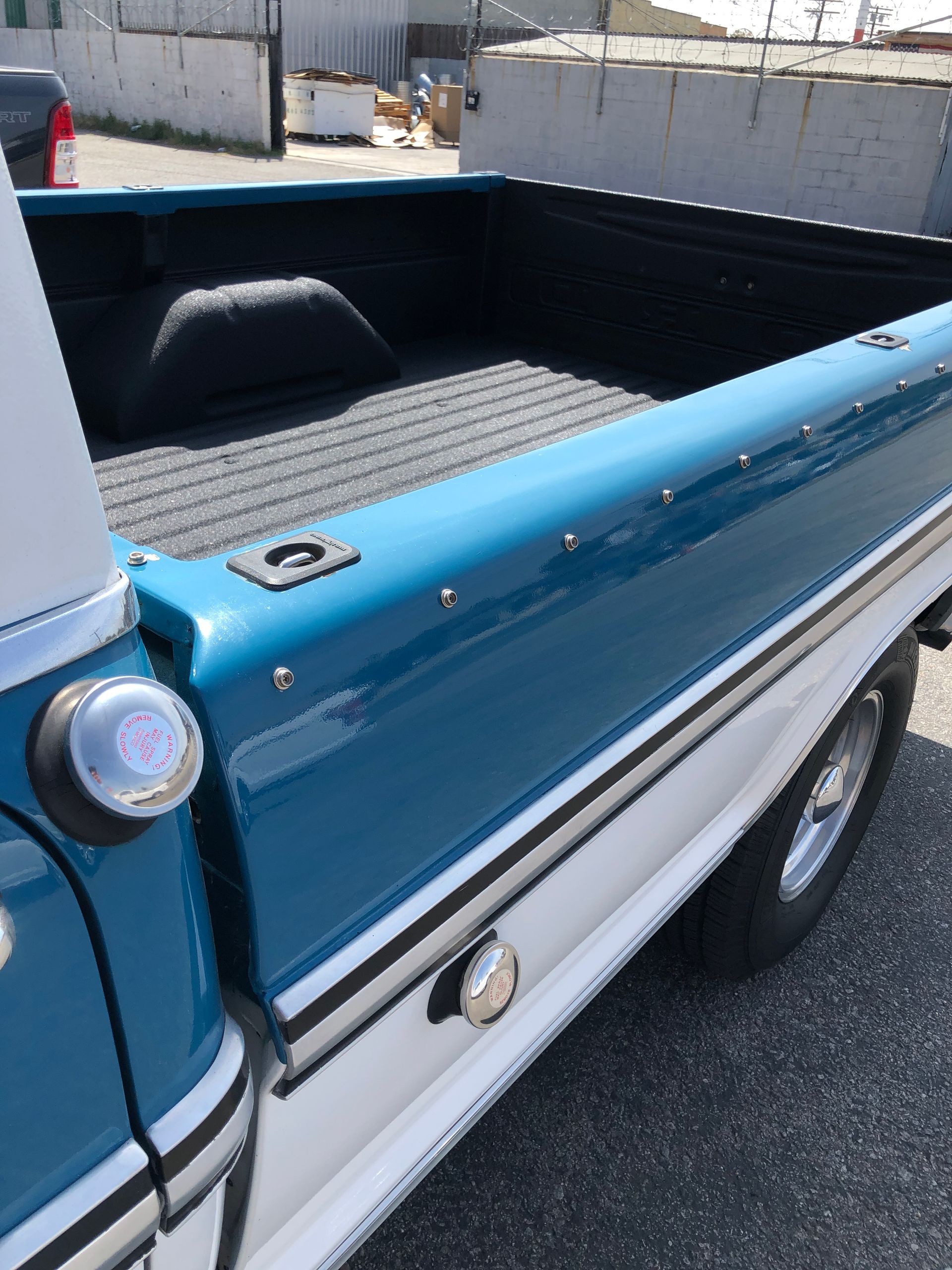 A view of the side and bed of a blue and white classic pickup truck with a black liner parked on asphalt.