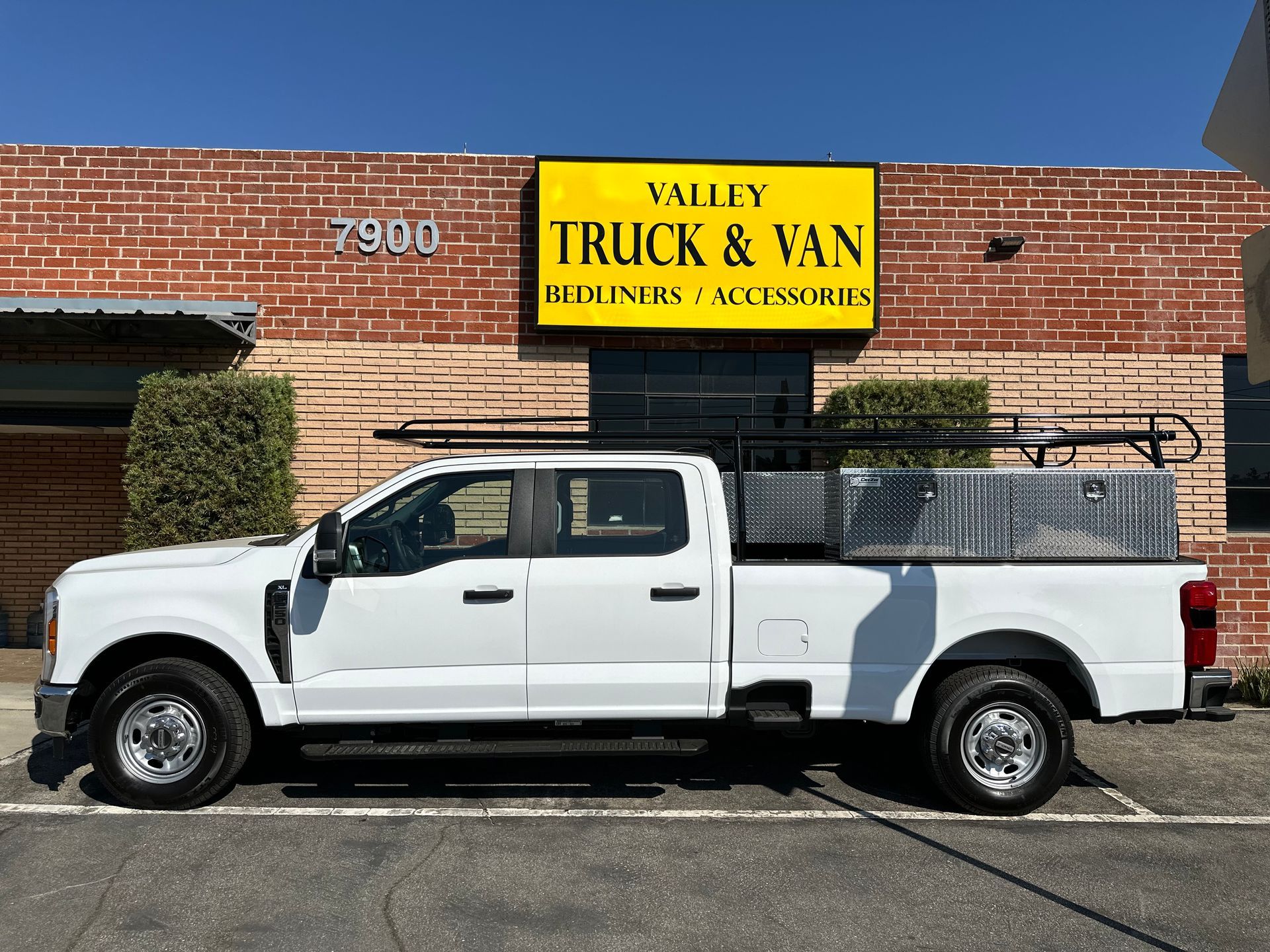 A white pickup truck with a utility rack and storage box parked in front of a brick building labeled Valley Truck & Van.