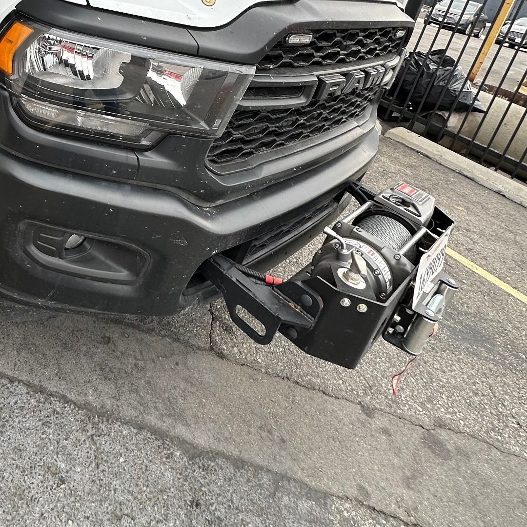 Front of white Ram truck with a winch attached to the bumper, parked on a street.