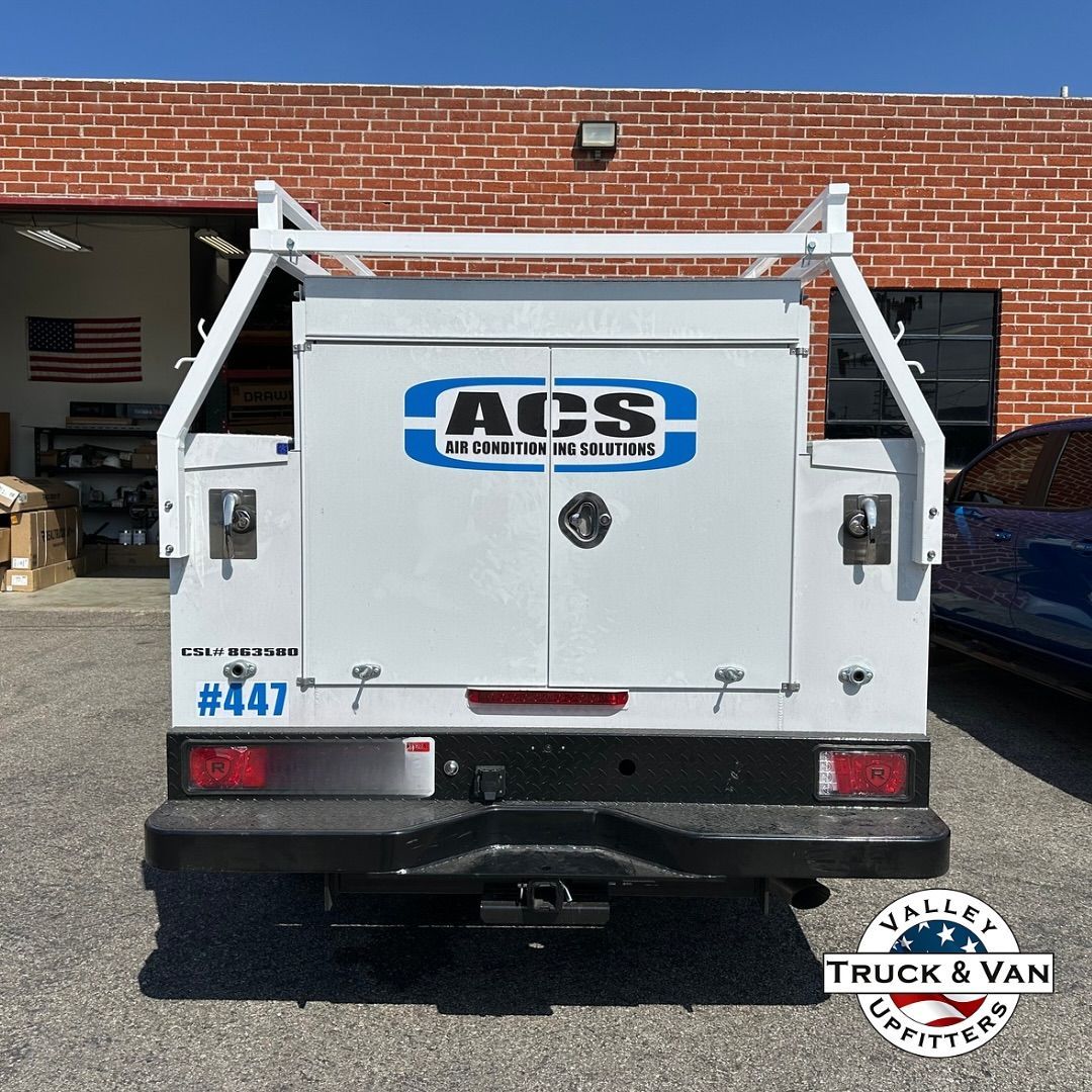 White utility truck with ACS Aluminum Buildings logo, ladder rack, and #447 against brick wall.