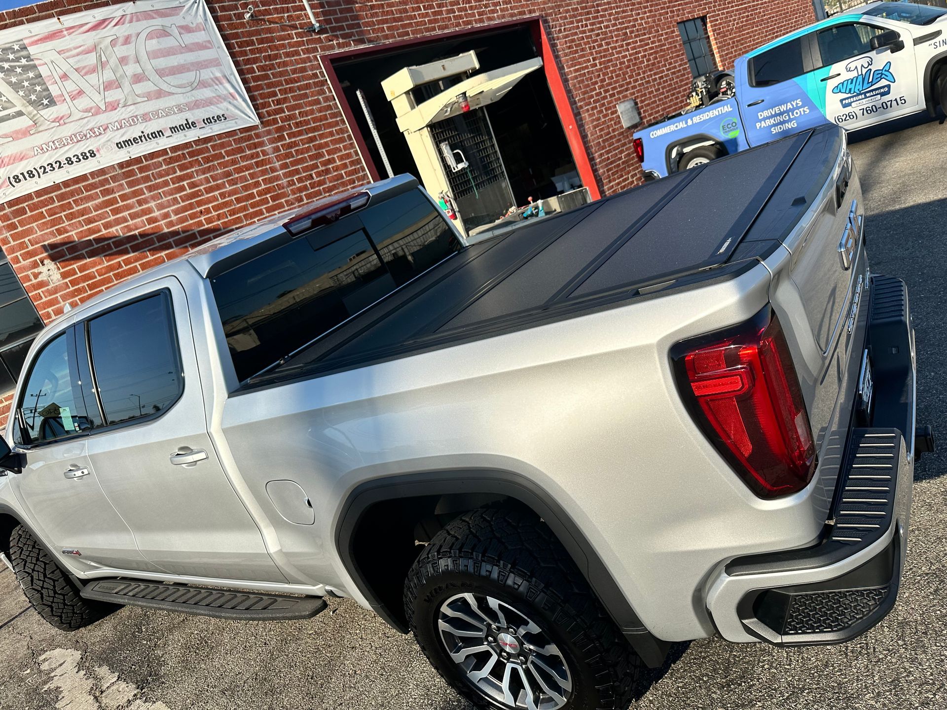 A silver pickup truck parked outdoors, featuring a black tonneau truck bed cover, captured at a high-angle rear view.