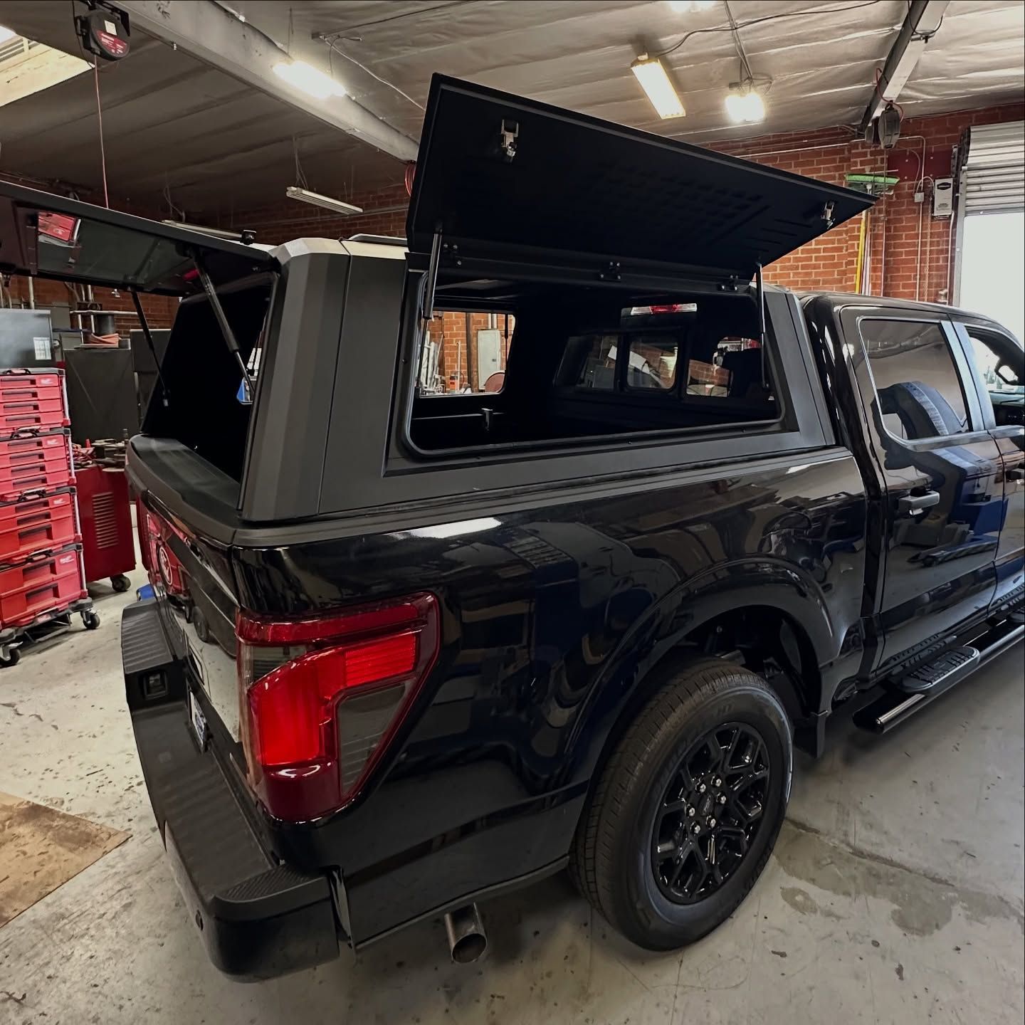 Black truck with a black cap, doors open in a garage.