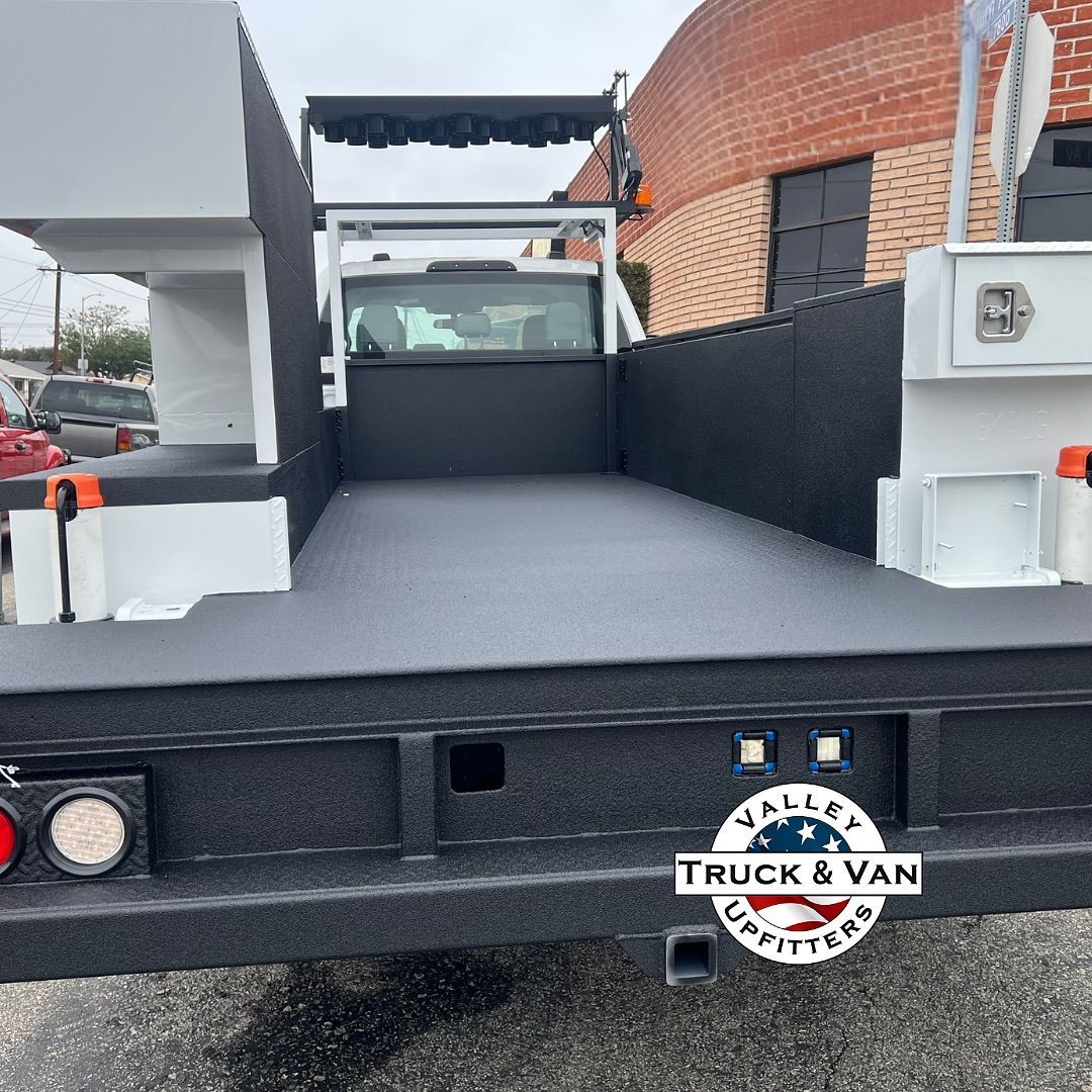 Black truck flatbed with a white truck cab. The bed has side compartments and a rack.