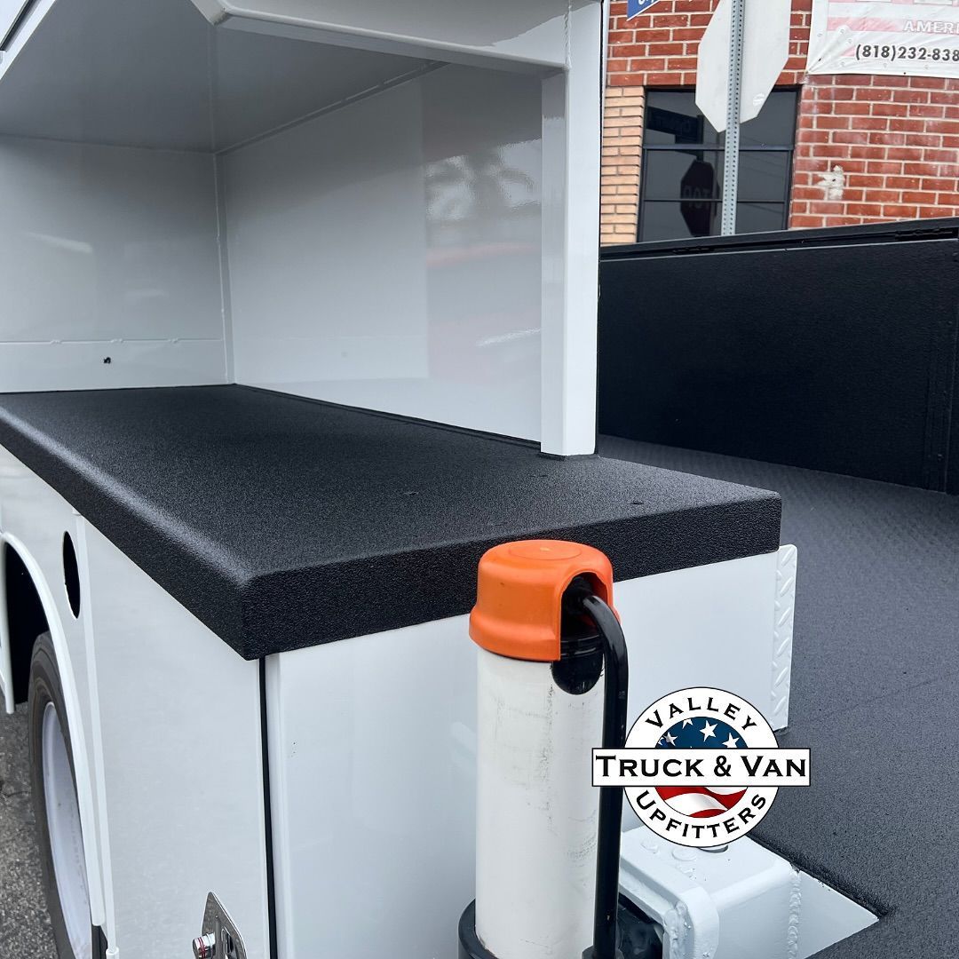White utility truck bed with a black rubberized surface; an orange cap is visible.