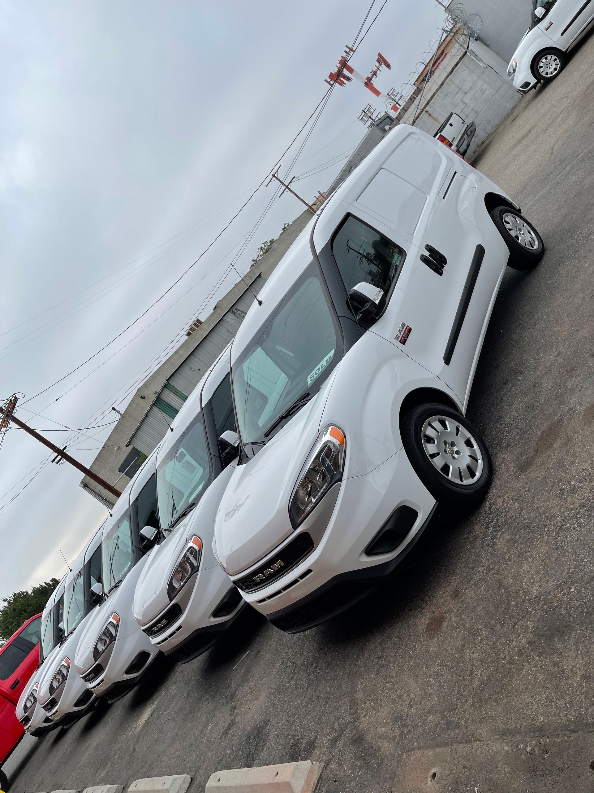 A line of white Ram ProMaster City cargo vans parked in an outdoor lot under a cloudy sky.
