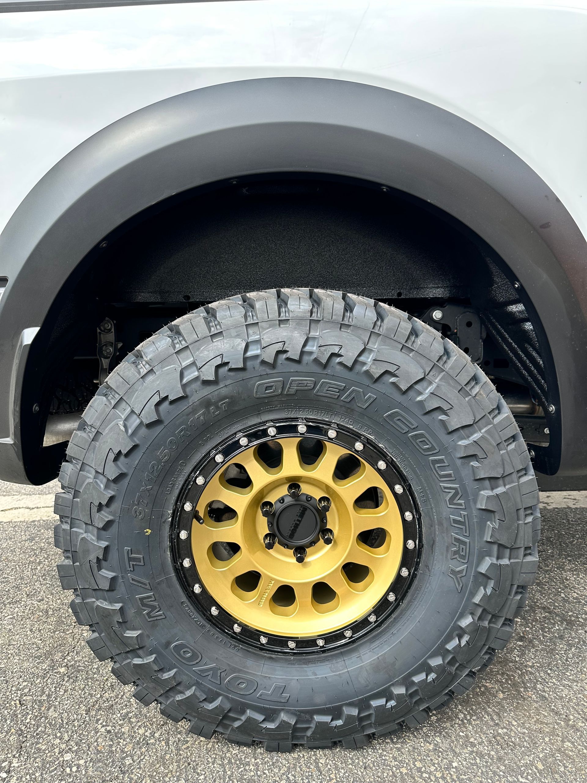 A close-up of a vehicle's large, textured off-road tire mounted on a gold rim with a black beadlock ring.