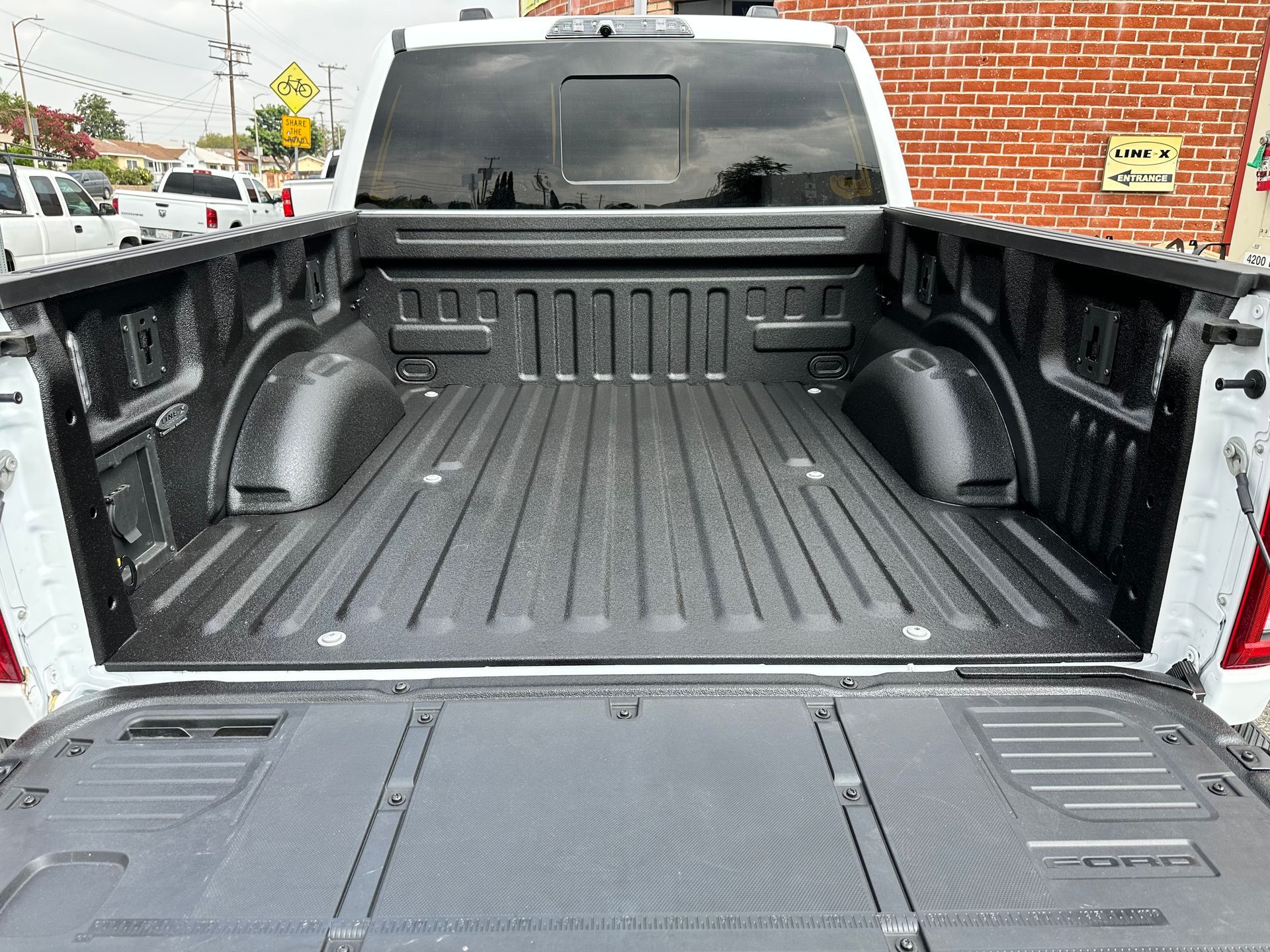 An open truck bed with a textured black spray-in liner, viewed from behind with the tailgate down.