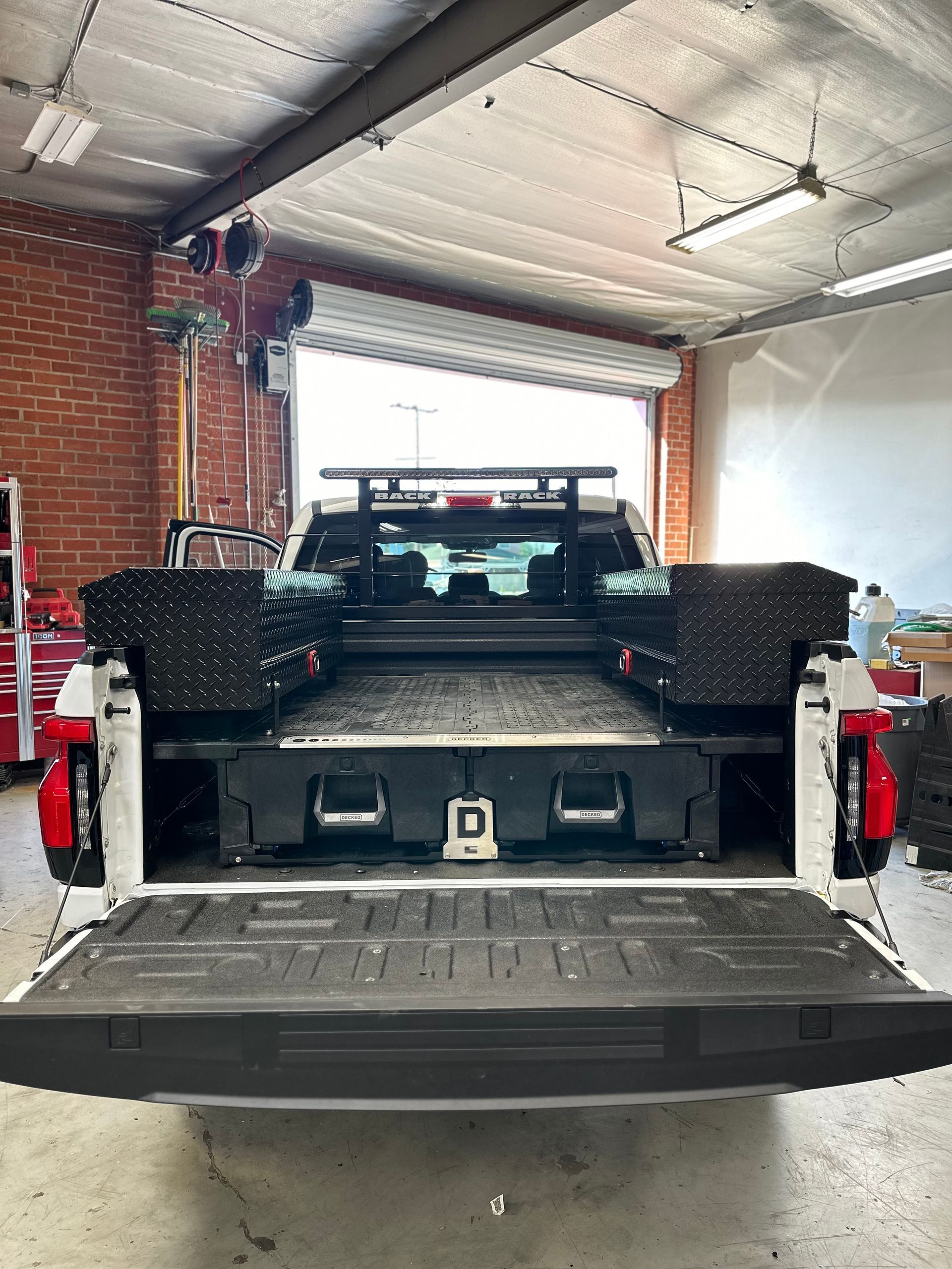 The open bed of a white pickup truck, equipped with black side-mounted toolboxes and a cargo storage drawer system.