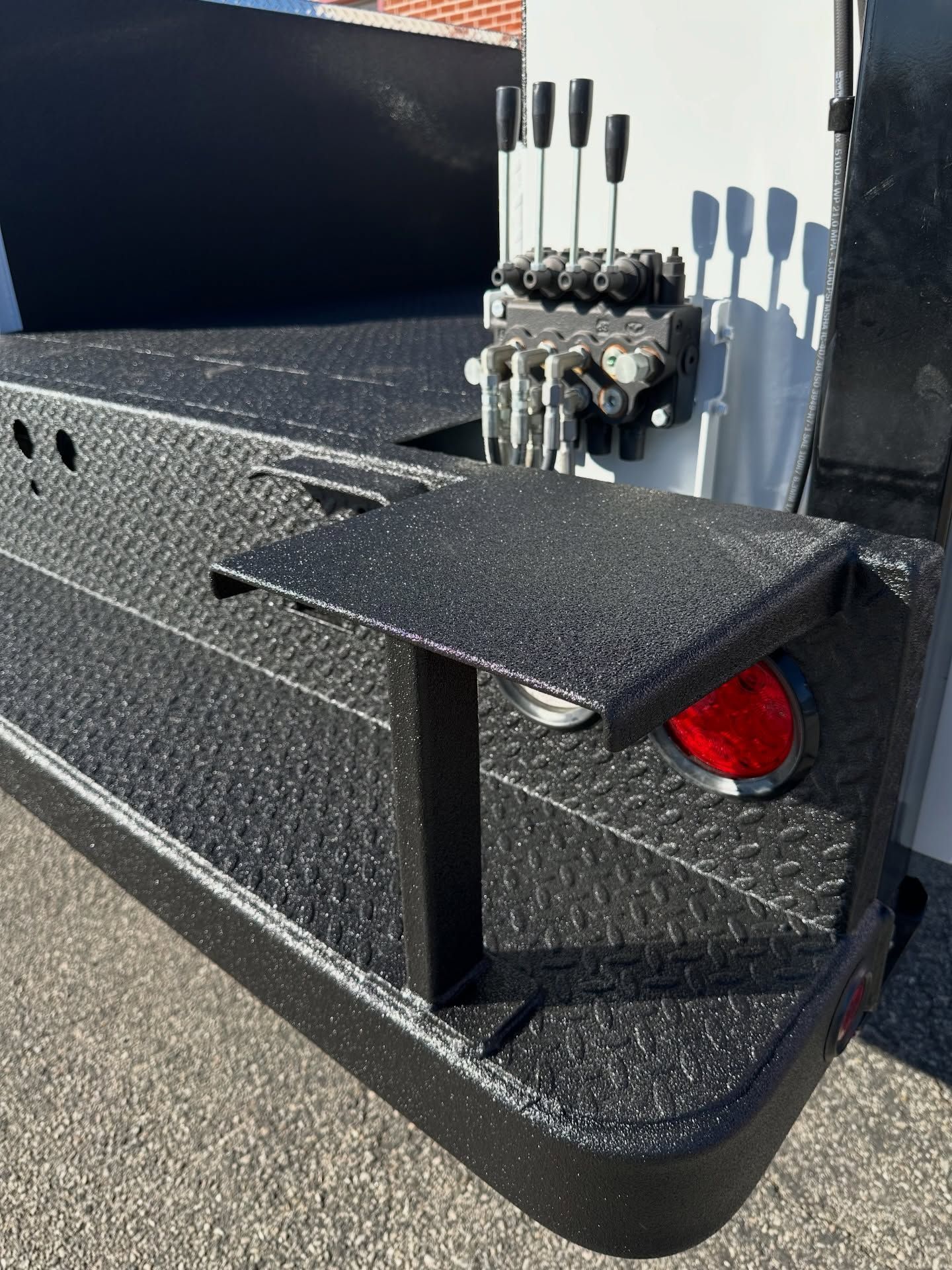 Black diamond-plate flatbed with a fold-down table, hydraulic controls, and a red taillight.